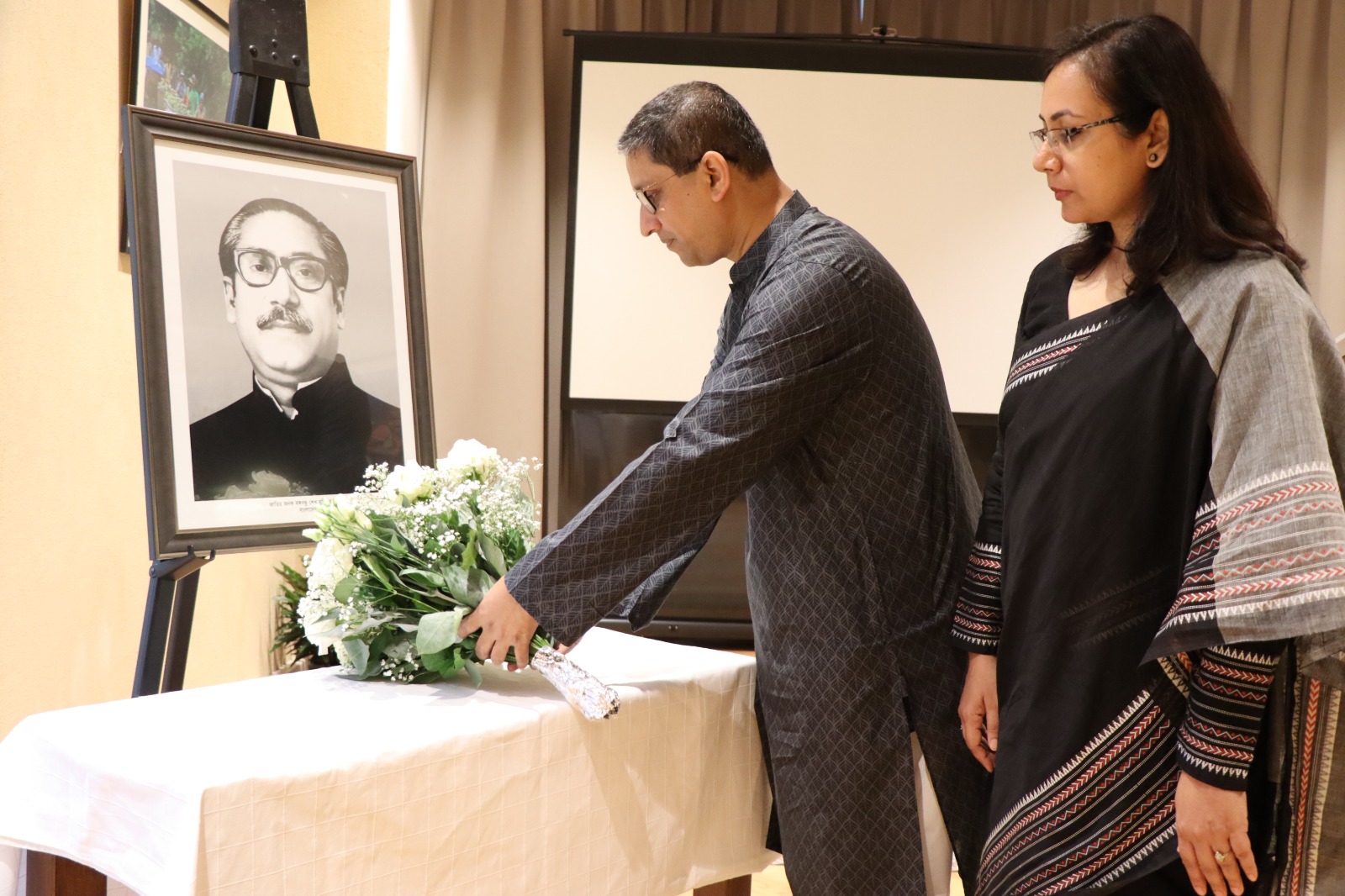 Ambassador and spouse placing a flower bouquet near images of the